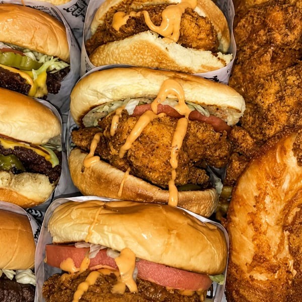 A cardboard box filled with six burgers, three beef and three fried chicken, alongside waffle fries.