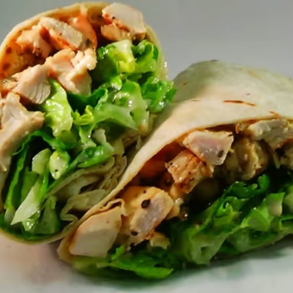 Two halves of a chicken Caesar wrap, filled with grilled chicken pieces and fresh green lettuce.