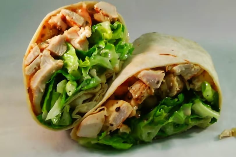 Two halves of a chicken Caesar wrap, filled with grilled chicken pieces and fresh green lettuce.