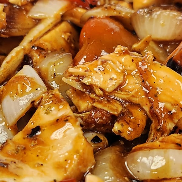 Close-up of chicken and vegetables in a rich, glossy sauce, featuring onions and red bell peppers.