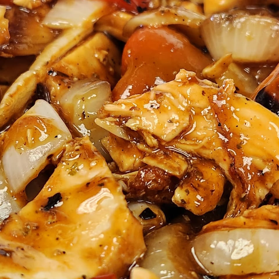 Close-up of chicken and vegetables in a rich, glossy sauce, featuring onions and red bell peppers.