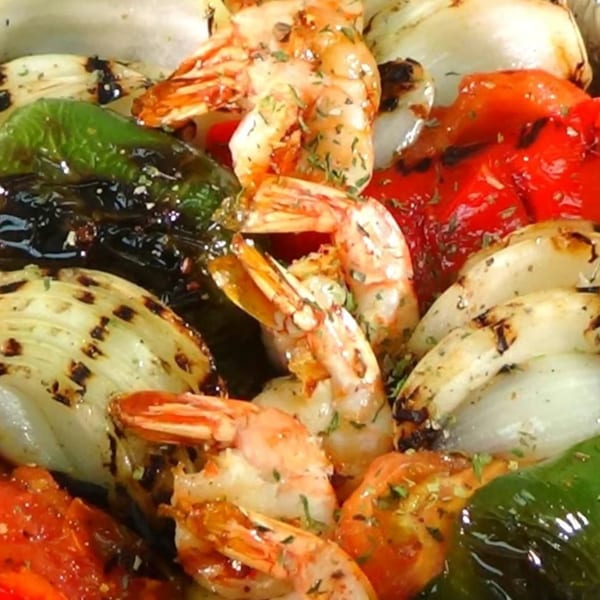 Close-up of grilled shrimp, red and green bell peppers, and onions seasoned with herbs.