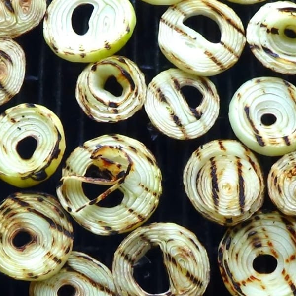 Grilled onion slices with char marks cooking on a black grill grate.
