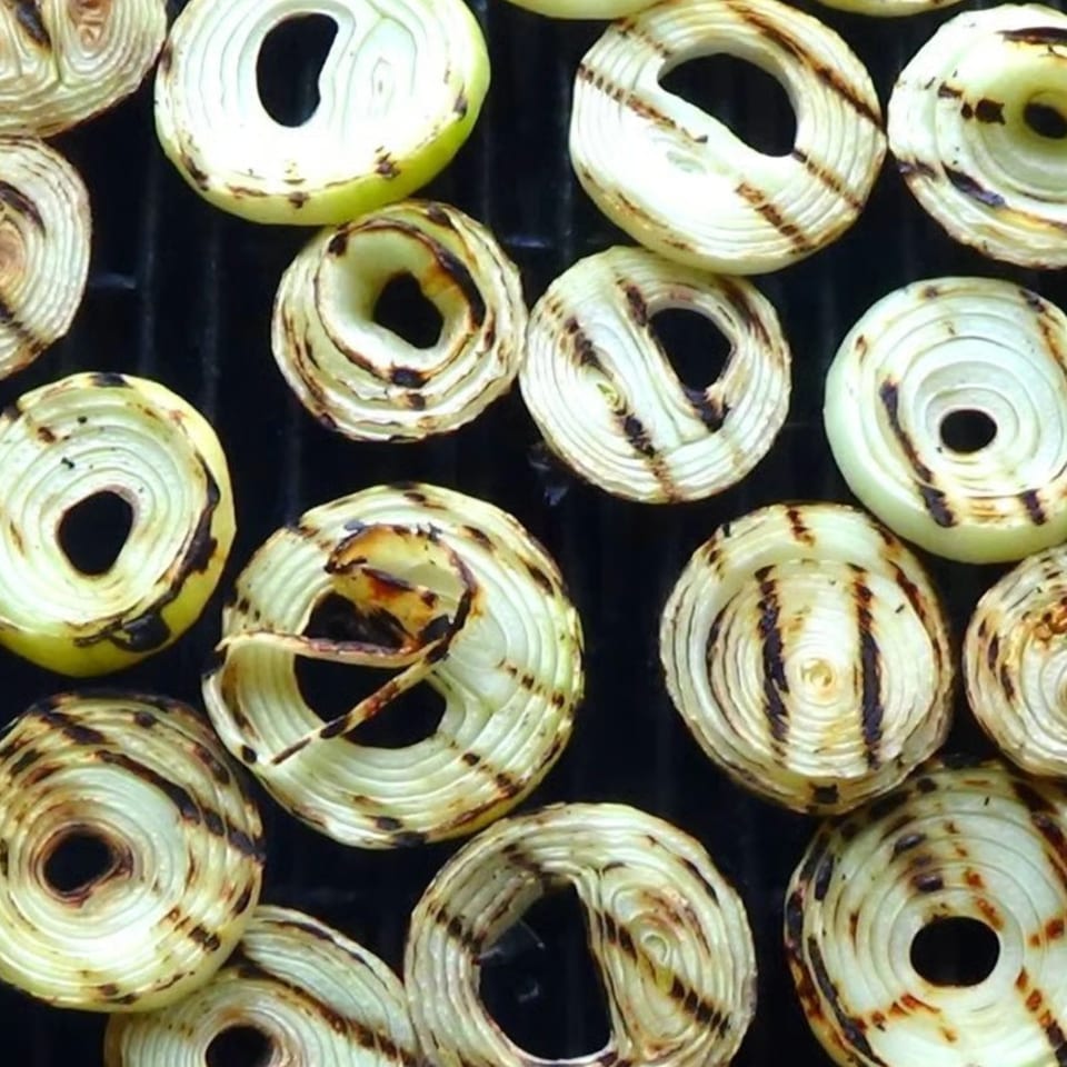 Grilled onion slices with char marks cooking on a black grill grate.