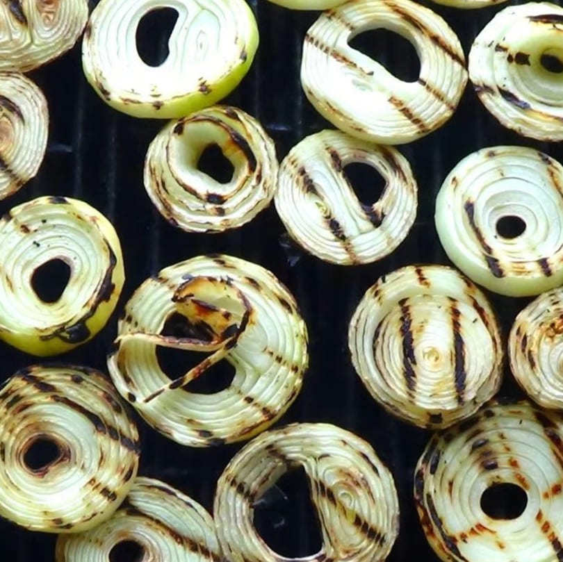 Grilled onion slices with char marks cooking on a black grill grate.